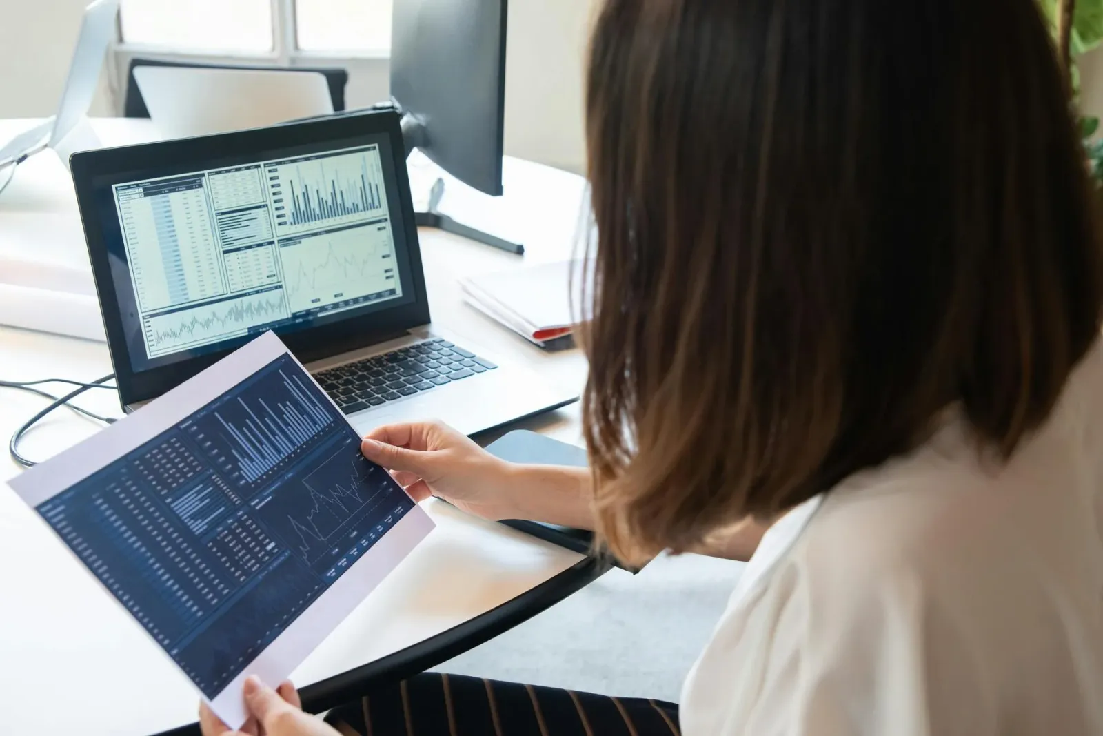 Personne qui analyse des graphiques de performance sur un écran et un document