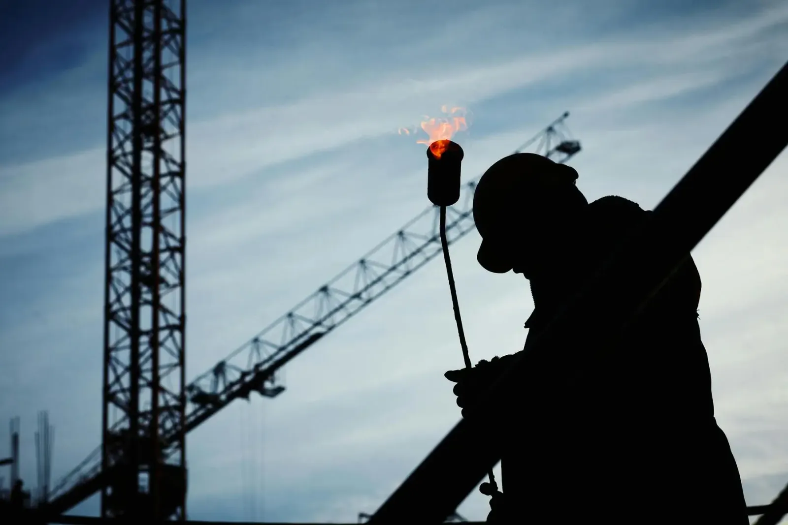Silhouette d’un ouvrier et d’une grue de chantier sur un ciel bleu